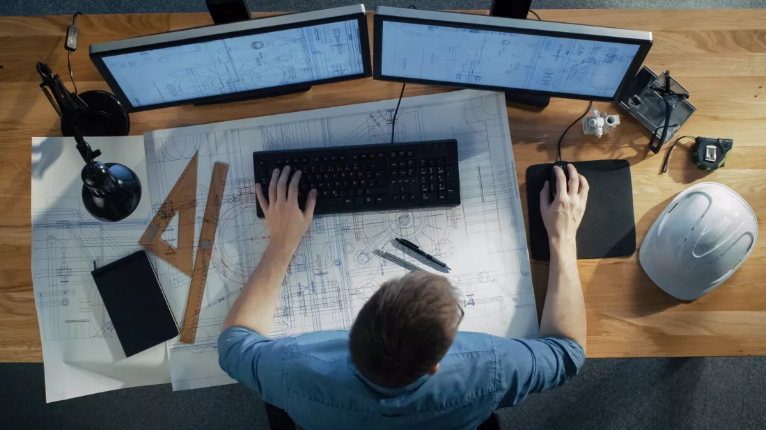 top-view-architectural-engineer-working-his-blueprints-holding-tablet-computer-using-desktop-computer-also-his-desk-is-full-useful-objects-evening-sun