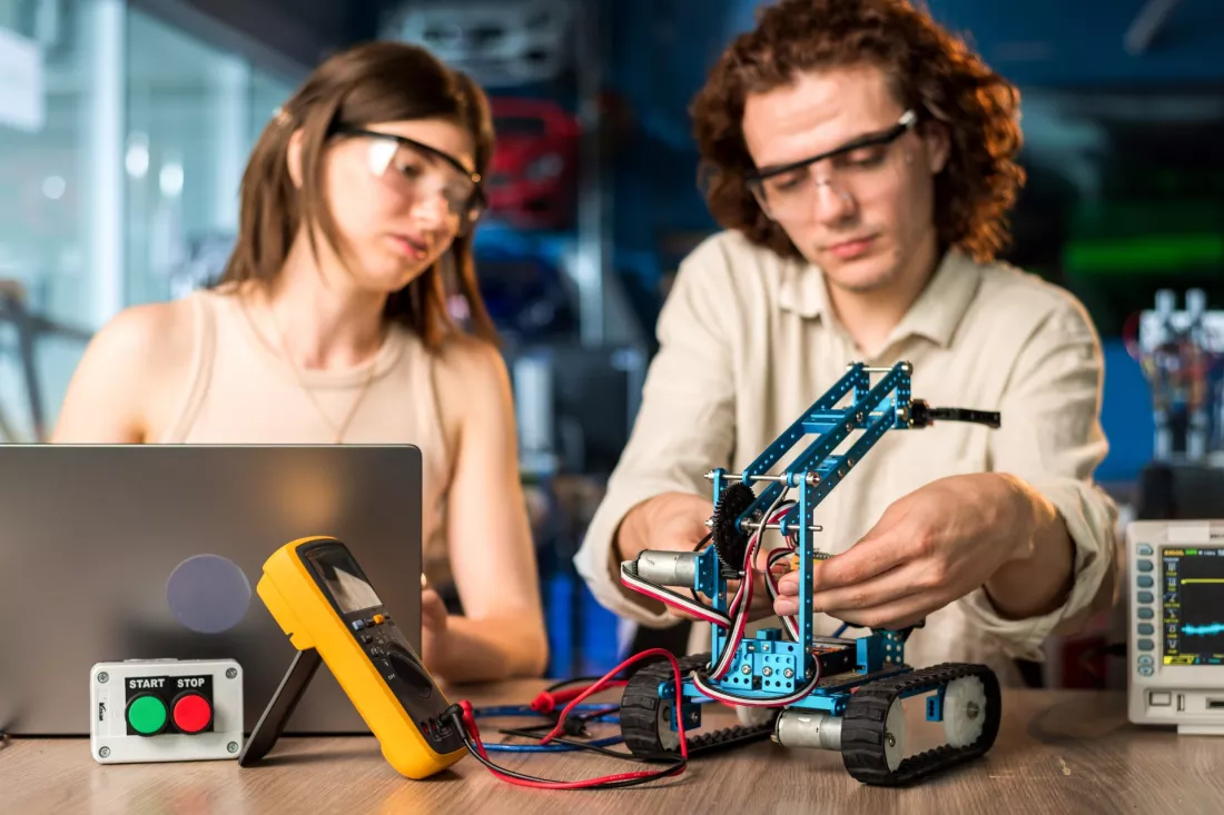 Studenci w okularach ochronnych programują robota gąsienicowego w laboratorium