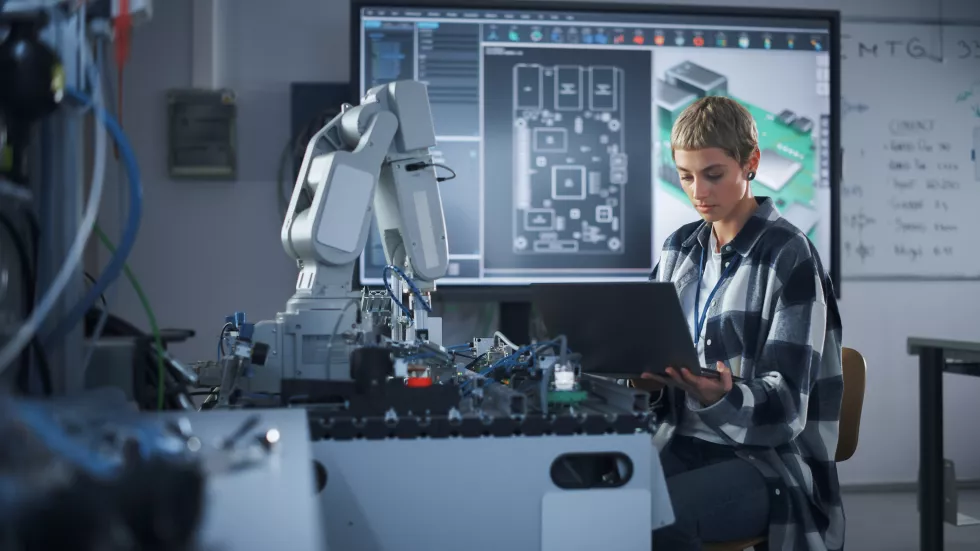 female-startup-developer-holding-laptop-while-working-with-robotic-arm-woman-looking-screen-programming-bionic-limb-hightech-science-research-university-lab-concept