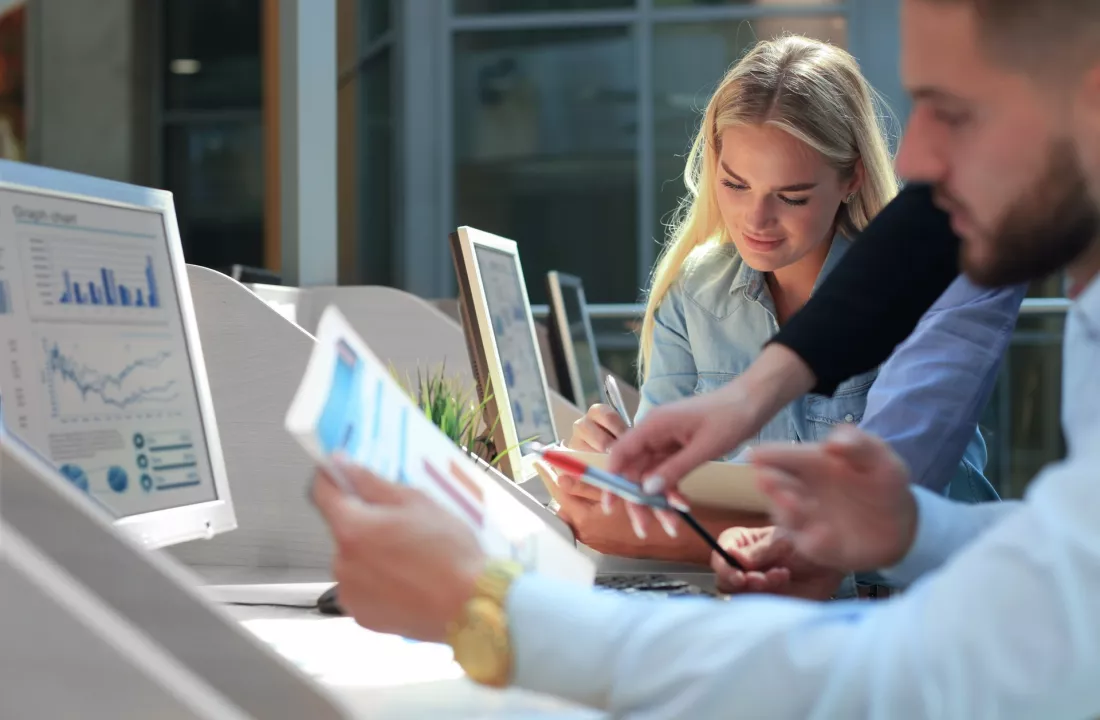 Młodzi ludzie wspólnie analizują wykresy na monitorze i tablecie.