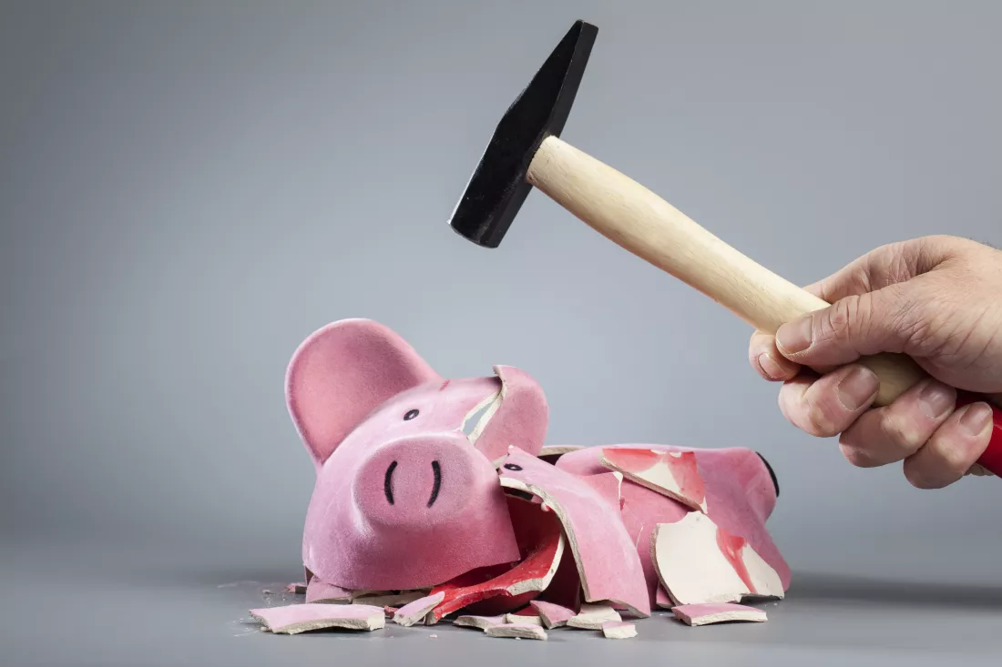 cropped-image-hand-breaking-piggy-bank-using-hammer-against-gray-background