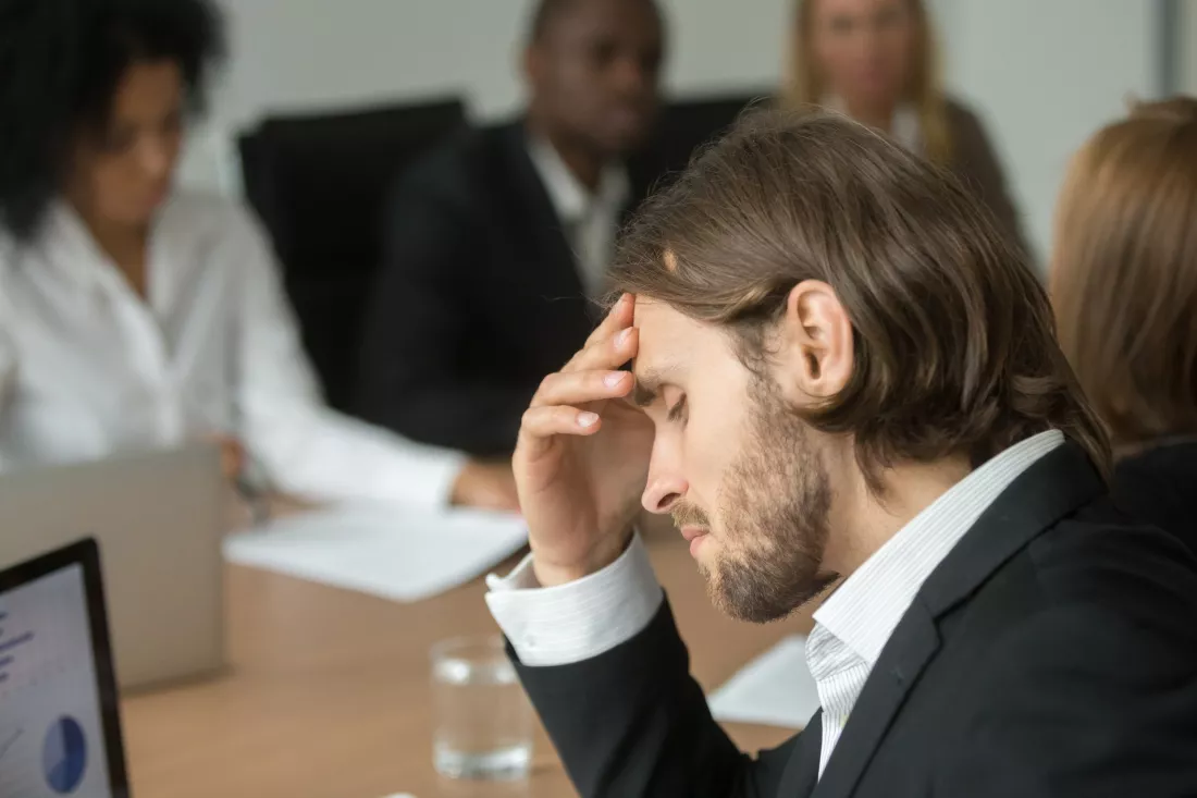 An exhausted employee holds his head in his hand during a team meeting in the office