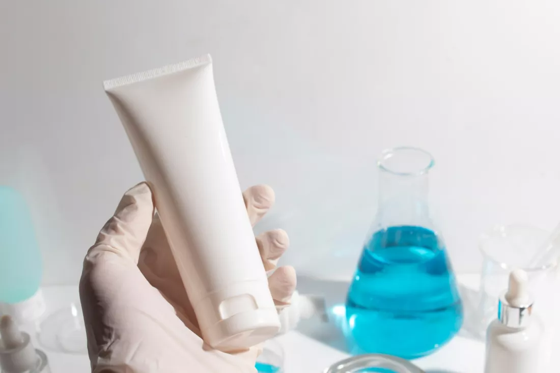 Dlon w rekawiczce trzyma tube kremu obok kolby w laboratorium kosmetycznym