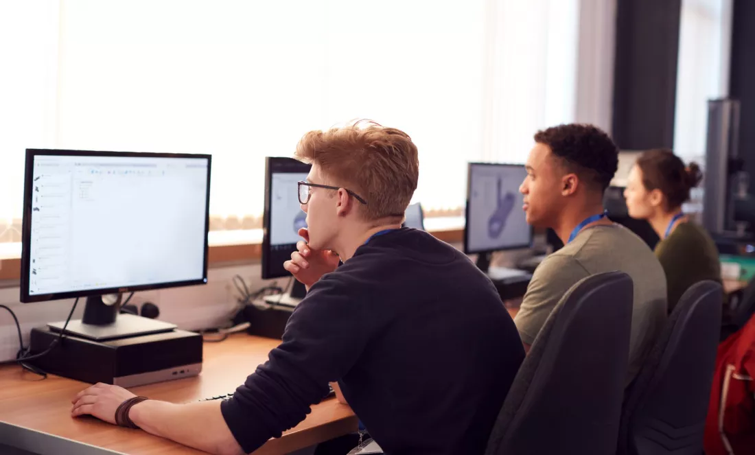 Studenci informatyki przy monitorach w uczelnianej pracowni komputerowej