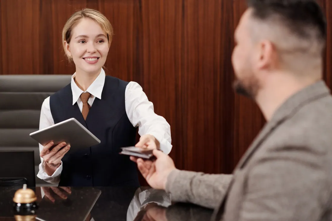 Młoda recepcjonistka w hotelu oddaje gościowi dokument przy ladzie recepcji